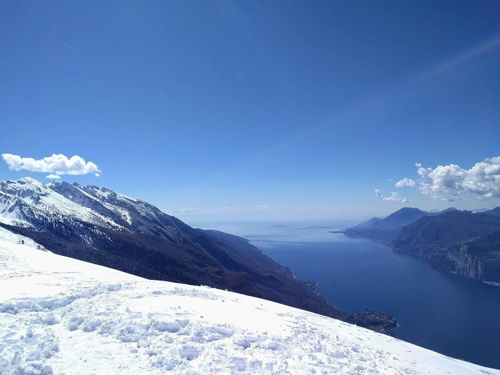Il Lago di Garda visto dalla cresta innevata del Monte Baldo in una giornata limpida di primavera