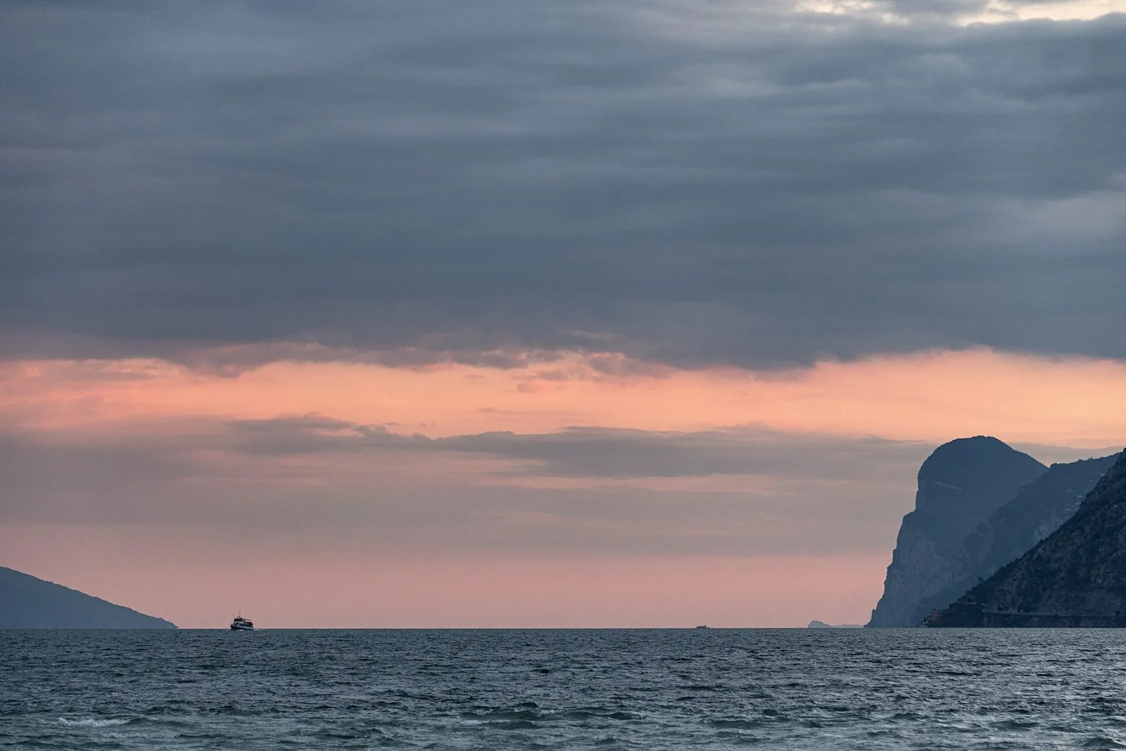 Cielo rosato e nuvole basse su una sera d'ottobre sul Lago di Garda, con un battello all'orizzonte
