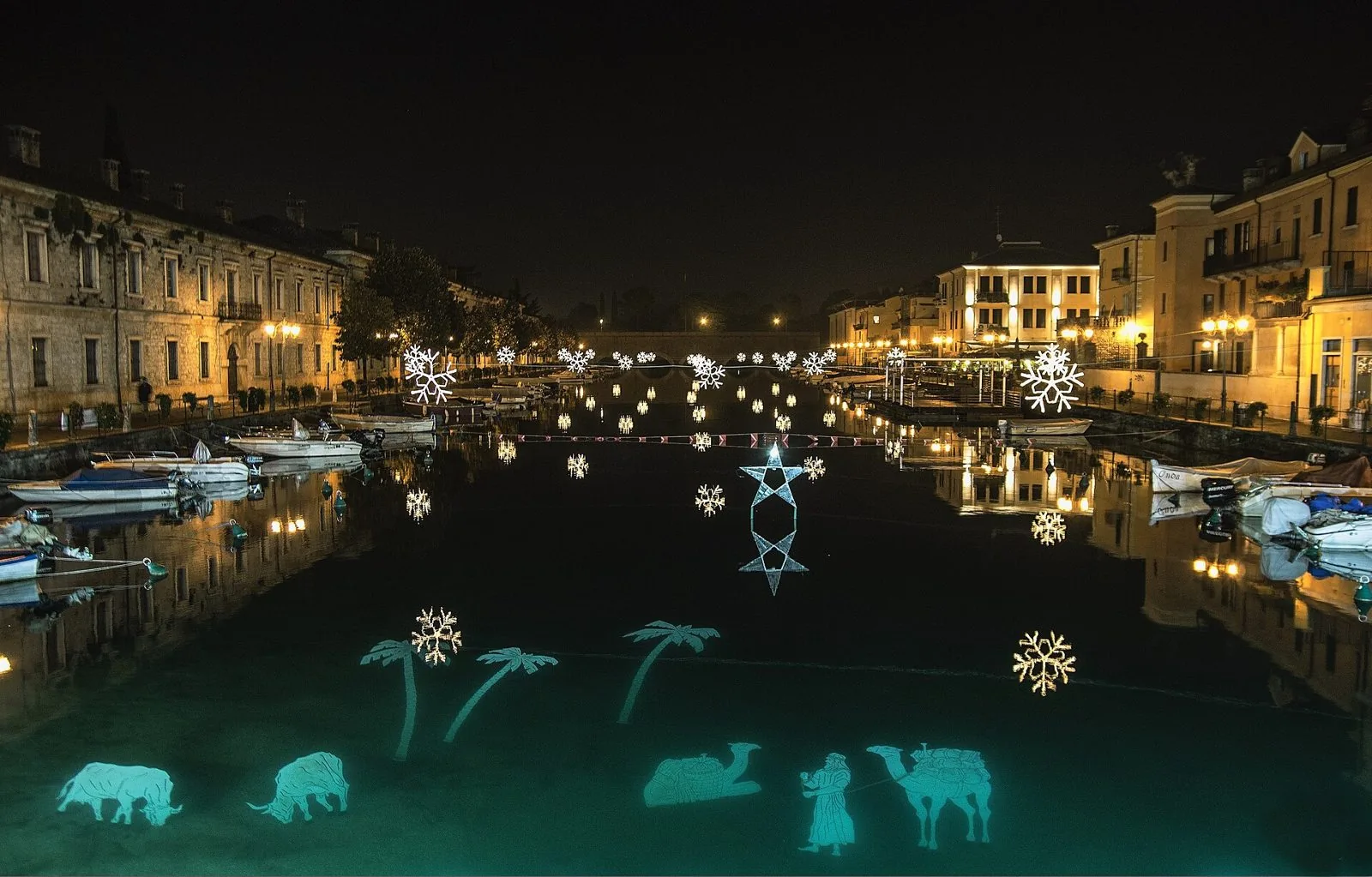 Il Canale di Mezzo di Peschiera del Garda di notte con gli addobbi natalizi e le figure luminose del presepe sull'acqua