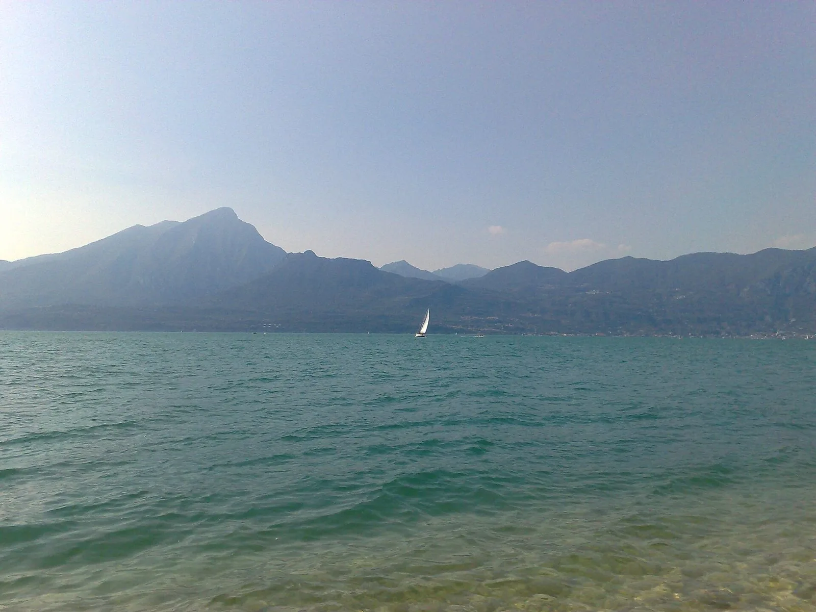 Il lago visto dalla spiaggia di Torri del Benaco, con una barca a vela e le montagne della sponda opposta